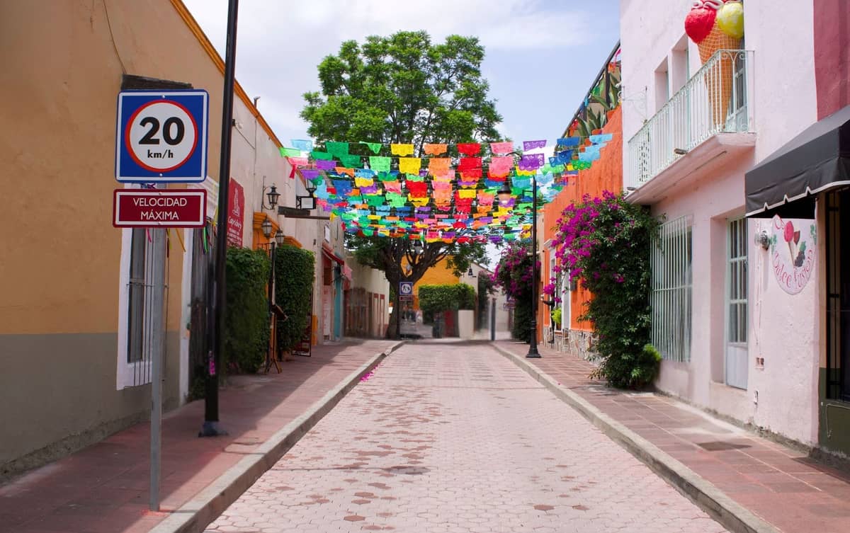 Kopfsteinpflasterstraße gesäumt von bunten Gebäuden und lebhaften Papel-Picado-Bannern über den Köpfen in einer kleinen mexikanischen Stadt.