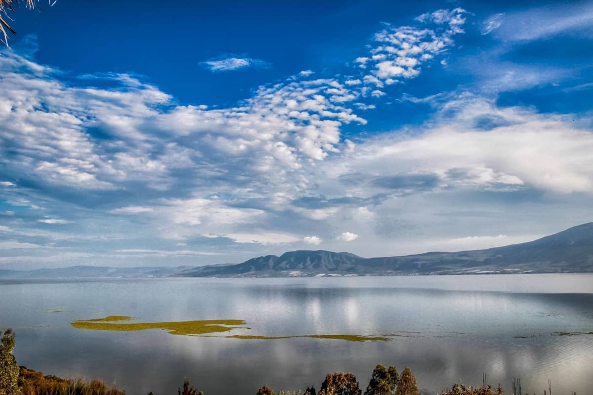Weitläufiger Blick auf den Lago Chapala mit Bergen in der Ferne und vereinzelten Wolken an einem hellen Tag.