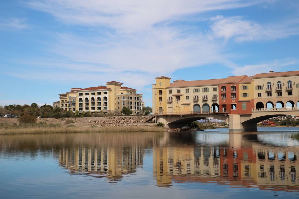 Tepi danau Lake Las Vegas dengan pantulan bangunan berwarna-warni dan jembatan lengkung di bawah langit biru.
