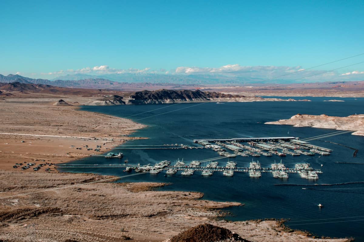 Foto panorâmica do Lago Mead mostrando a margem desértica, a água azul intensa e várias marinas com barcos, destacando a área de recreação e o reservatório.