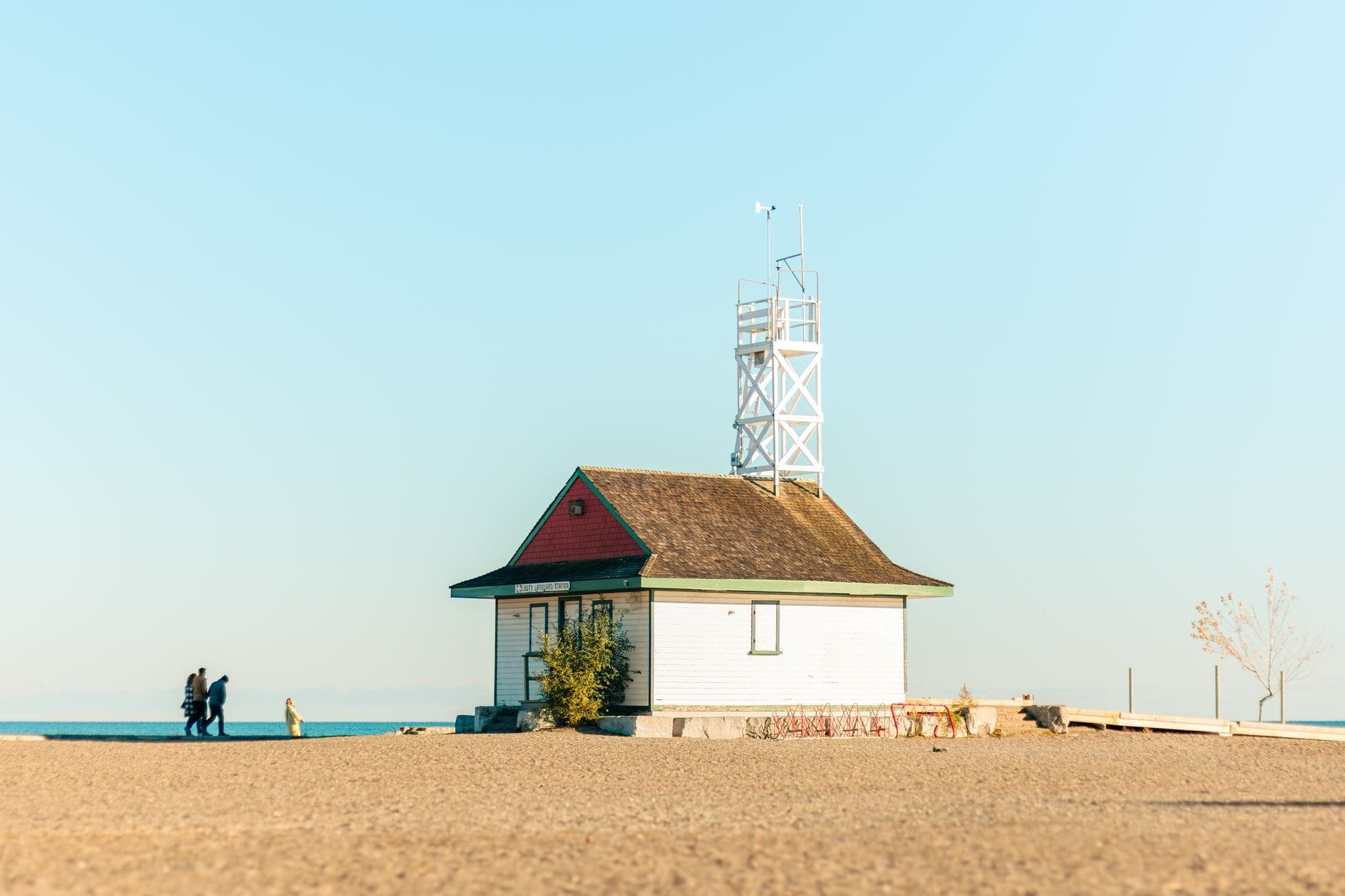 Uma praia de areia com a icônica Leuty Lifeguard Station e algumas pessoas caminhando perto do lago Ontario em um dia claro.