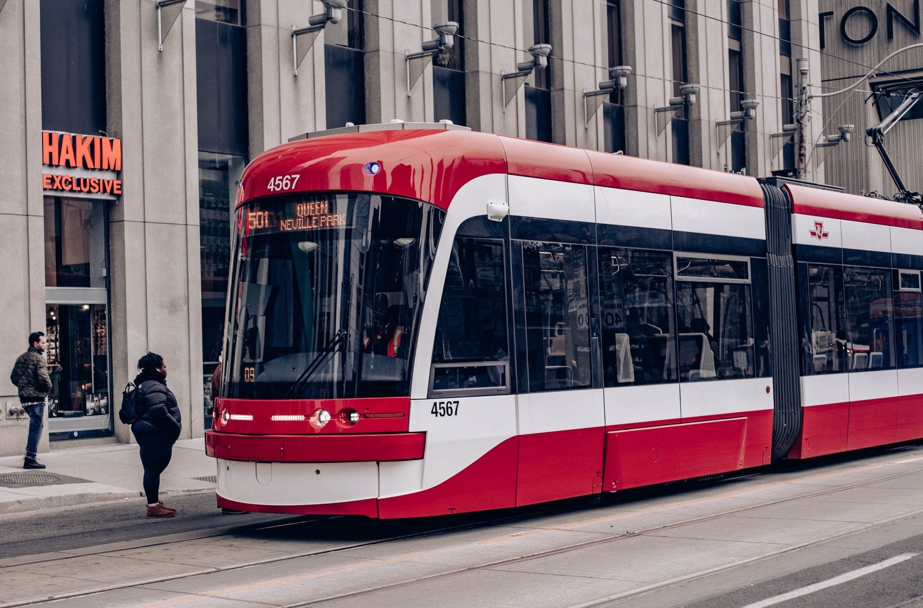 Bonde de Toronto parado em uma plataforma no centro da cidade com pessoas embarcando e desembarcando em uma rua urbana.