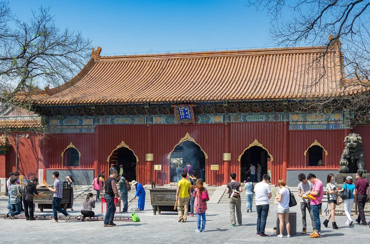 Besucher und Gläubige versammeln sich vor der Haupthalle des Lama-Tempels in Beijing, mit aufwendigen roten Fassaden unter einem klaren blauen Himmel.