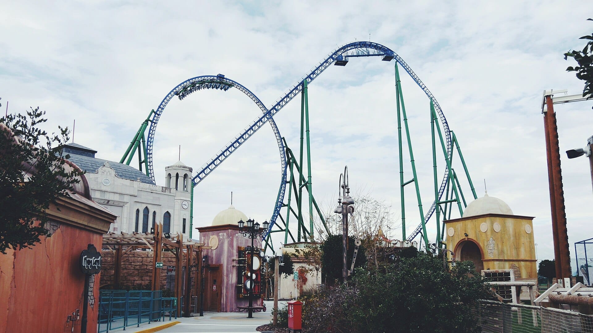 Alta pista di montagne russe blu e verde con loop dietro edifici a tema ornati al Land of Legends Theme Park ad Antalya sotto un cielo nuvoloso.