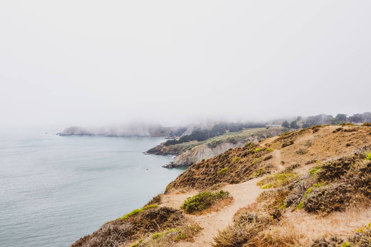 Sentiero costiero avvolto nella nebbia su una scogliera selvaggia sopra il Pacifico, con percorsi sterrati sinuosi e falesie spettacolari a Lands End, San Francisco.