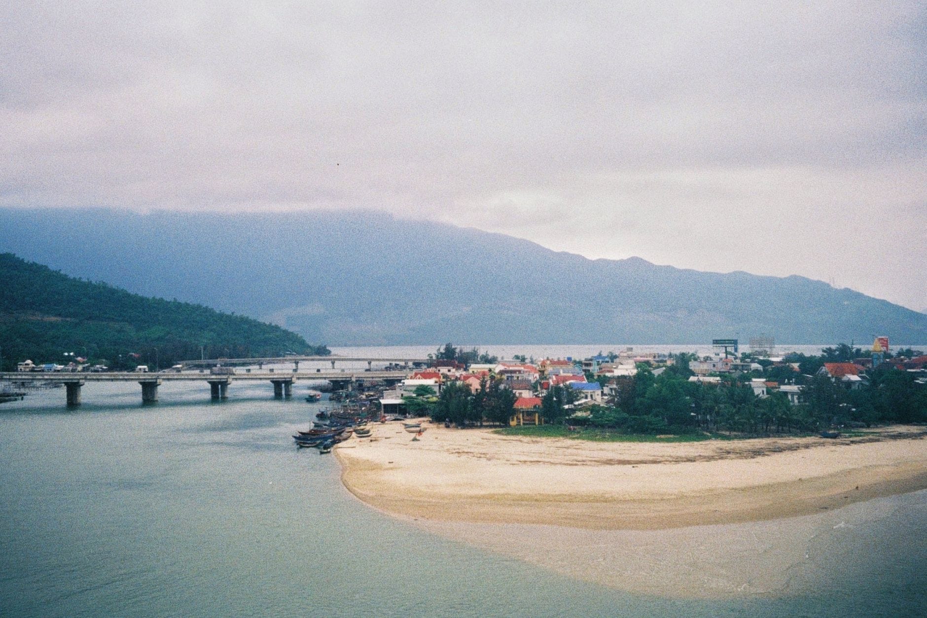 วิวอ่าวลังโกกับหาดทรายขาว ทะเลสาบ สะพาน และภูเขาในฉากหลัง มีเมฆครึ้ม สะท้อนบรรยากาศเฉพาะตัวของอ่าวเหนือด่านหายเวิน