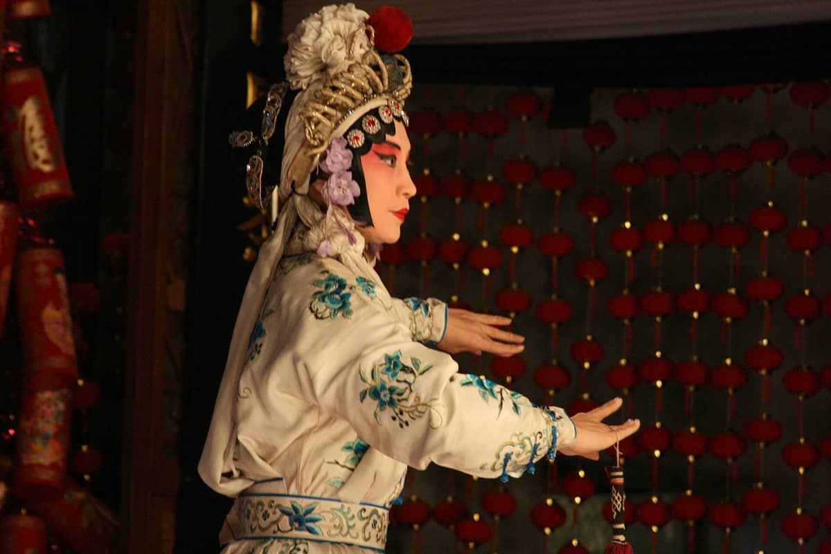 Peking-Oper-Darsteller in aufwendigem Kostüm und traditioneller Maske auf der Bühne des Lao She Teehauses, mit roten Laternen im Hintergrund.