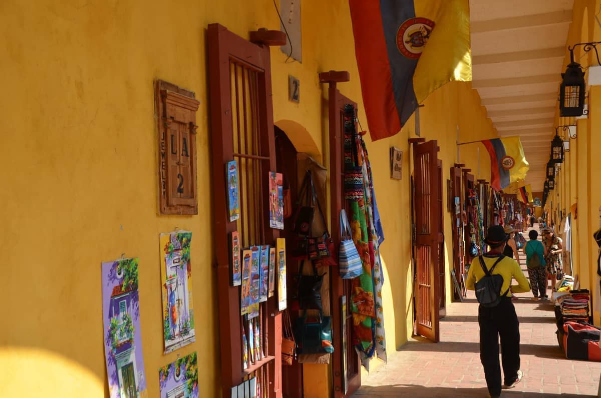 Colorful craft shops and Colombian flags line the yellow arched corridor of Las Bóvedas in Cartagena, with paintings and textiles on display.