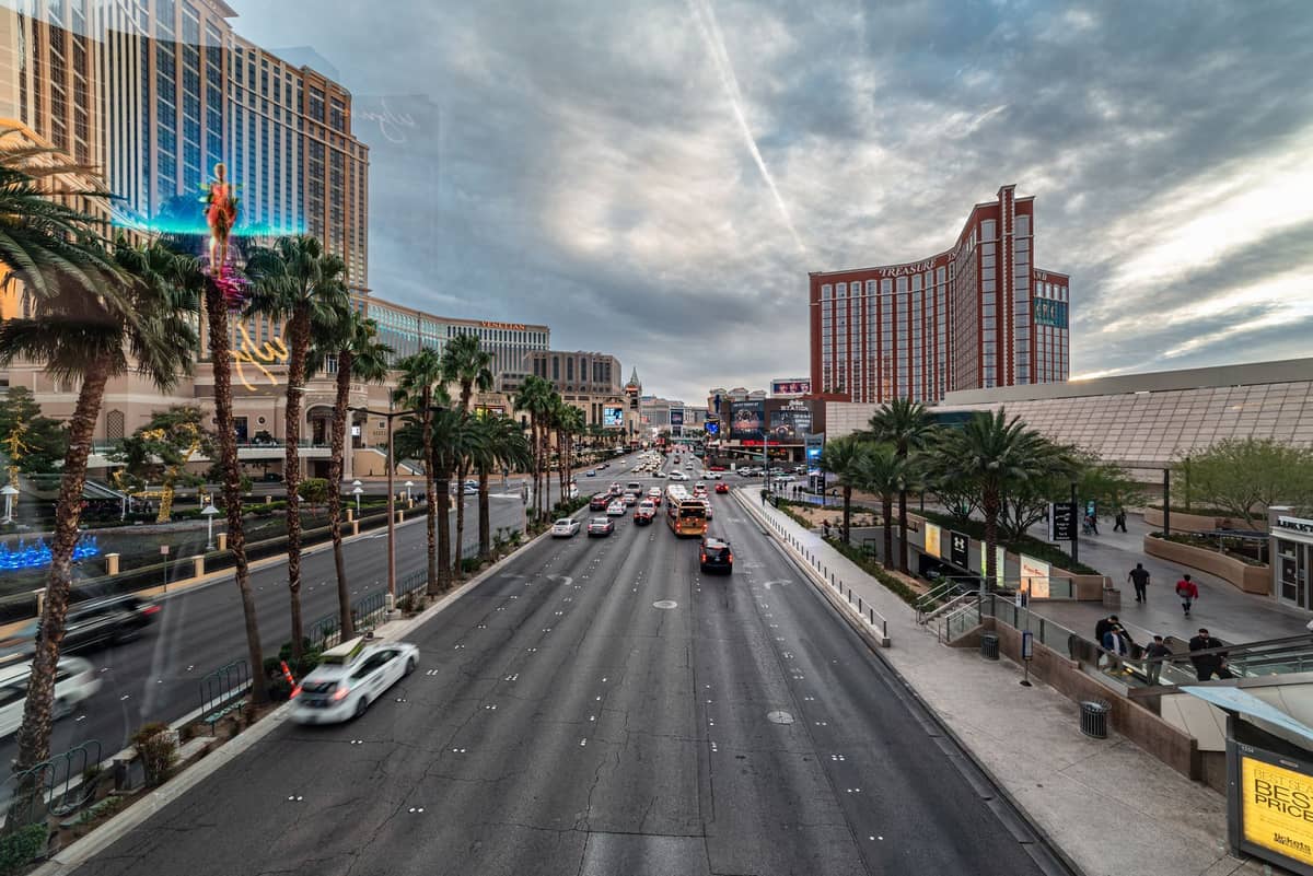 วิวกว้างของ Las Vegas Strip พร้อมรถยนต์และต้นปาล์ม แสดงให้เห็นถนนหลายช่องจราจรที่คับคั่งซึ่งเรียงรายด้วยโรงแรมและคาสิโนชื่อดังในเวลากลางวัน