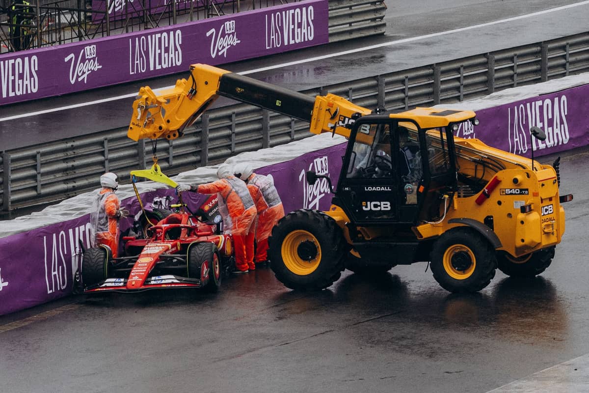 Formula 1 car being lifted by a crane after an accident on the Las Vegas Grand Prix circuit, with purple Las Vegas barriers and track marshals.