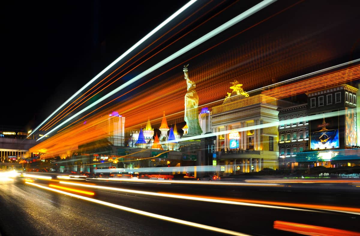 Langzeitbelichtung von Autos, die Lichtspuren auf dem Las Vegas Strip bei Nacht erzeugen, mit beleuchteten Hotels und den Wahrzeichen des New York-New York im Hintergrund.
