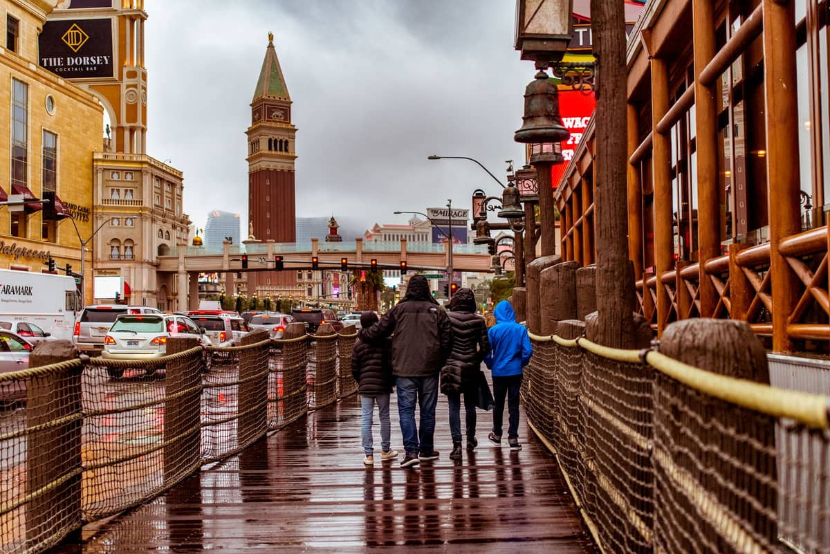 Menschen in Jacken und Mänteln spazieren auf dem Las Vegas Strip in der Nähe des Venetian, mit sichtbaren Restaurants und Geschäften an einem bewölkten Tag.