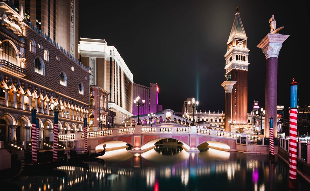 Vista nocturna de The Venetian y su réplica del Gran Canal, puente y campanario en el Strip de Las Vegas, con vibrantes luces reflejadas en el agua.