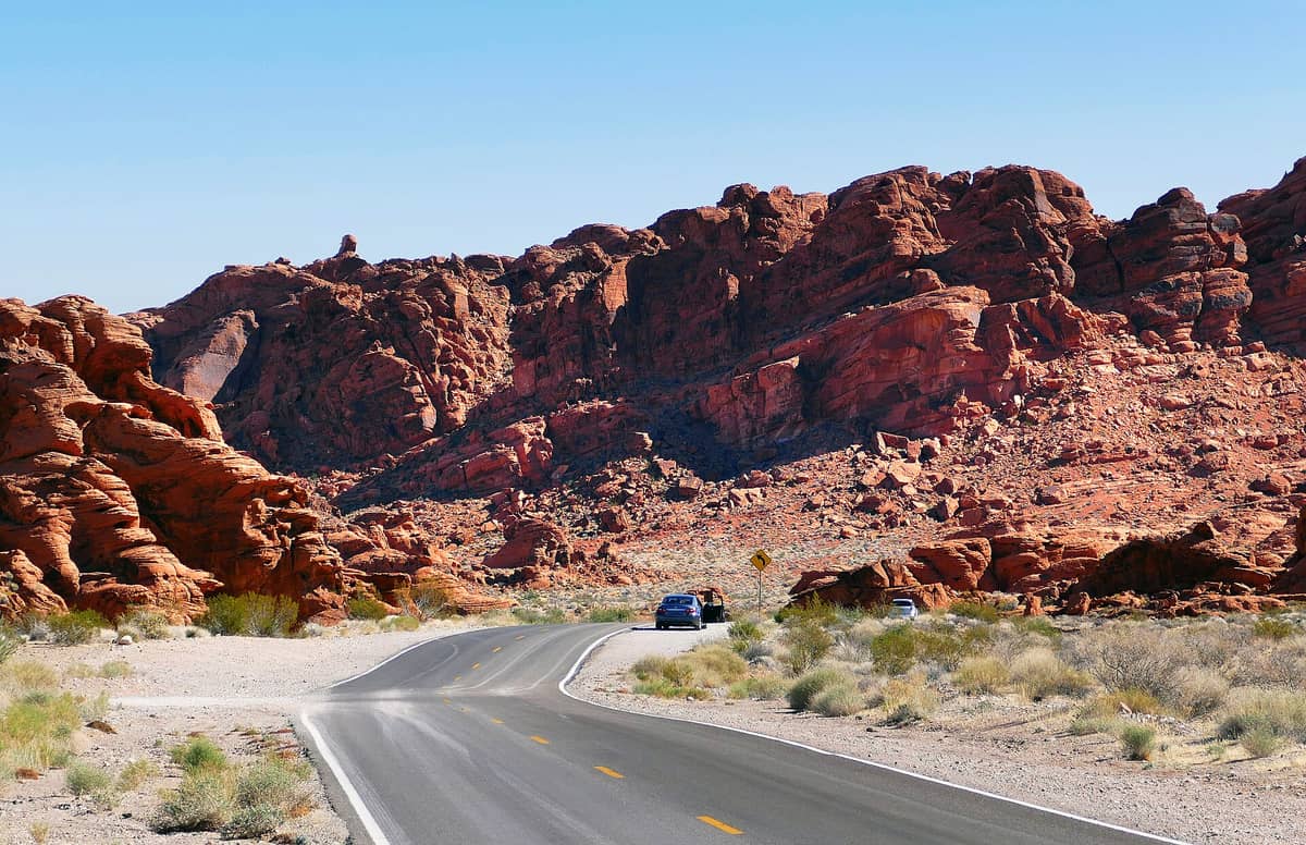 Jalan berkelok-kelok dengan mobil melewati formasi batu merah yang dramatis di bawah langit biru cerah dekat Las Vegas