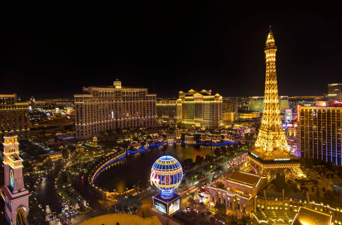 Aerial night view of the Las Vegas Strip showing Bellagio fountains, Paris Hotel Eiffel Tower replica, and neon lights along the boulevard.