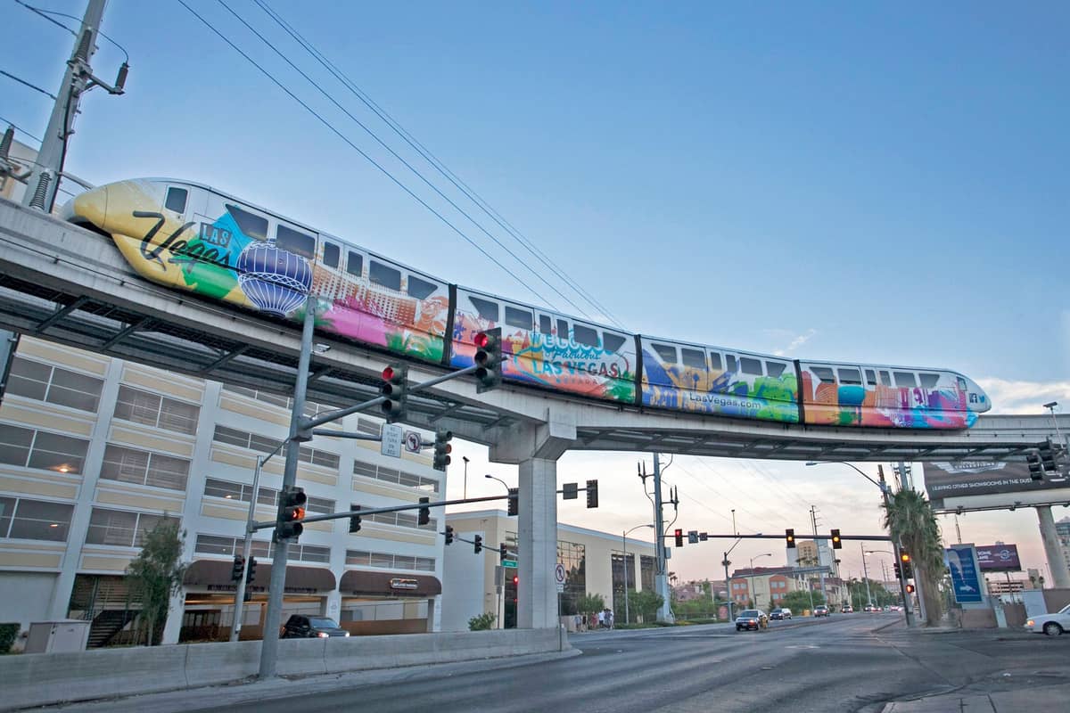 The Las Vegas Monorail train traveling on an elevated track above a city street with hotels in the background.