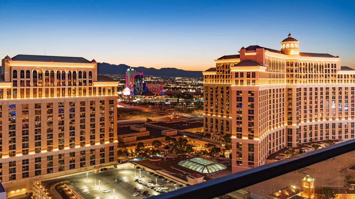 วิวยามเย็นของหอคอยโรงแรม Bellagio ที่สว่างไสวบน Las Vegas Strip พร้อมแสงไฟของเมืองและภูเขาที่อยู่ไกลออกไป