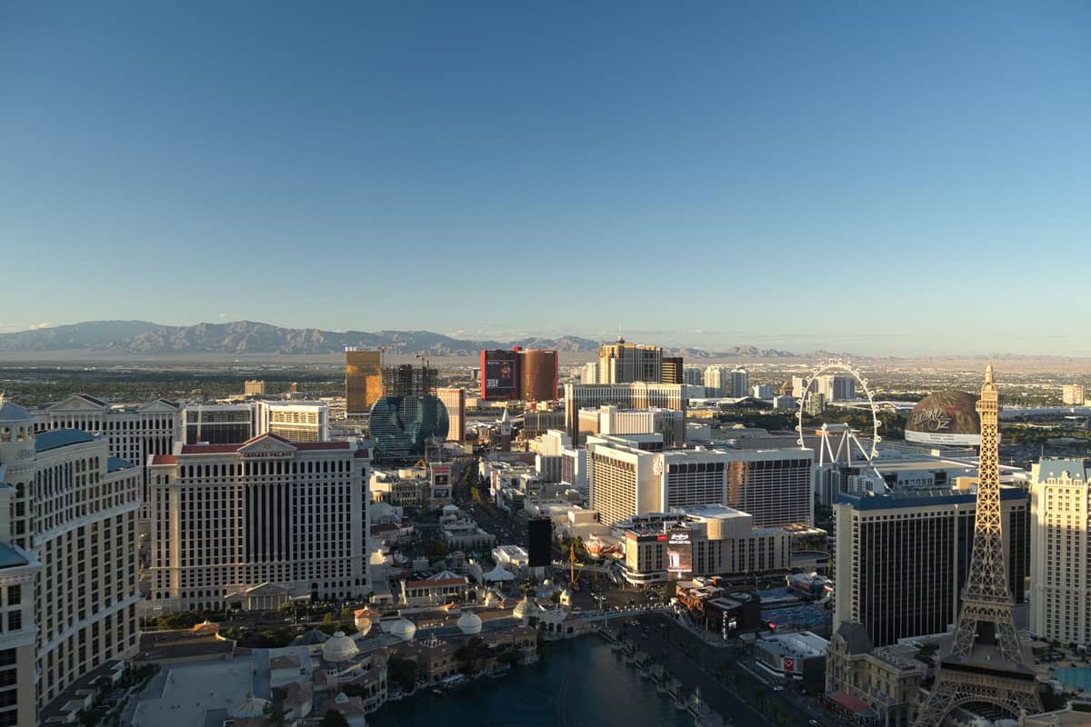 มุมมองจากที่สูงของโรงแรมและคาสิโนบน Las Vegas Strip ใต้ท้องฟ้าสีฟ้า พร้อมรีสอร์ตชื่อดังและเส้นขอบฟ้าของเมืองในเวลากลางวัน