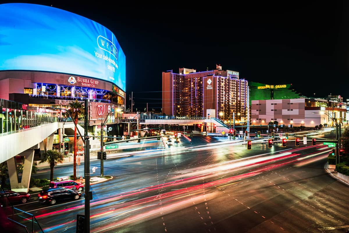 Vista del Strip de Las Vegas de noche con luces brillantes, una gran valla publicitaria digital y casinos y hoteles icónicos visibles.