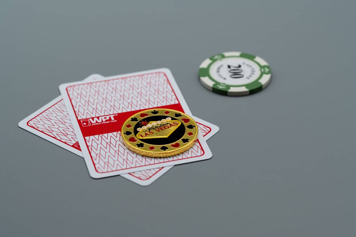 Close-up of two playing cards, a poker chip labeled Las Vegas, and another casino chip on a grey table.
