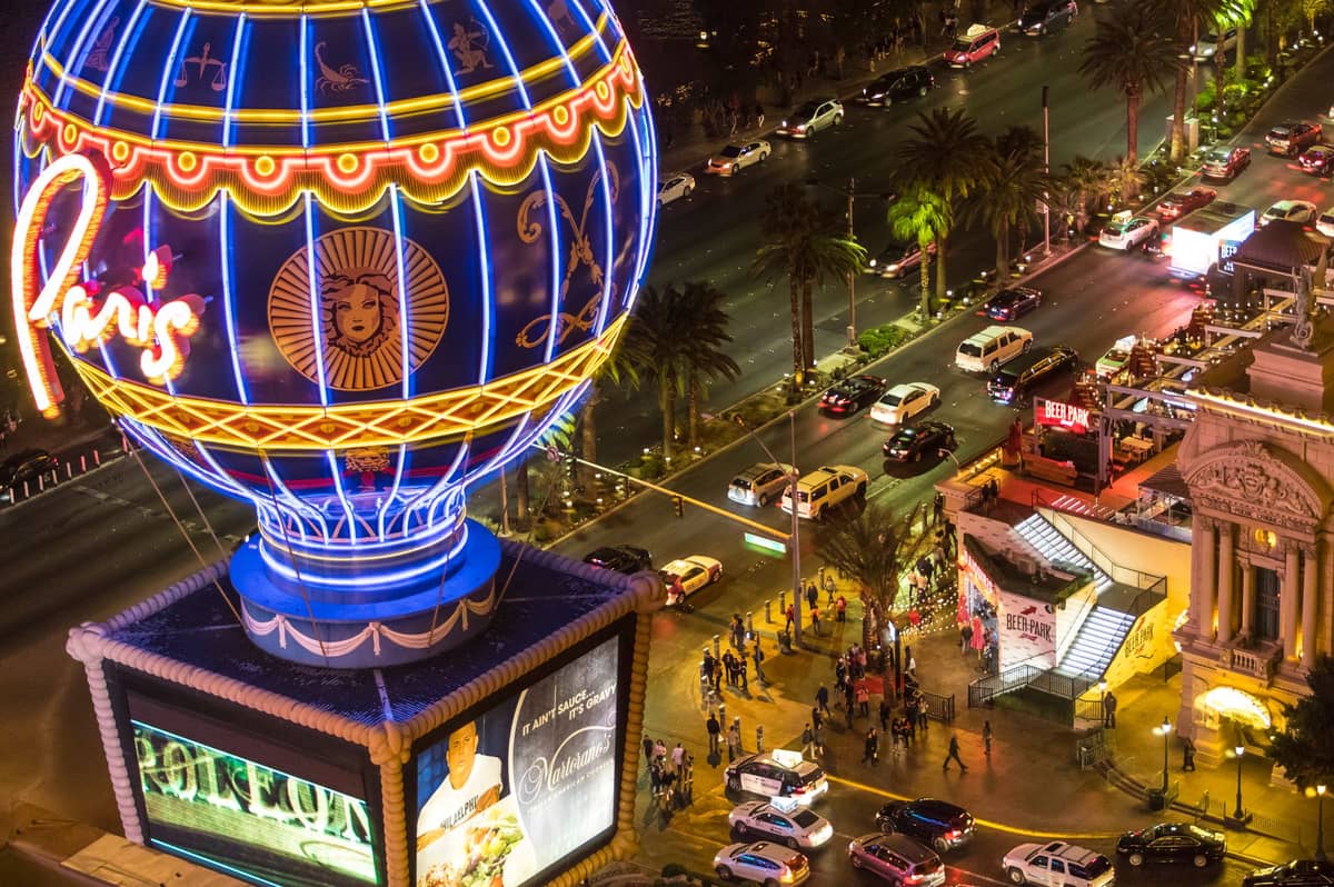 Nächtliche Luftaufnahme des Las Vegas Strip mit Menschenmassen, Neonlichtern, Autos und dem Ballon des Paris Las Vegas, die eine belebte Veranstaltungsatmosphäre zeigt.
