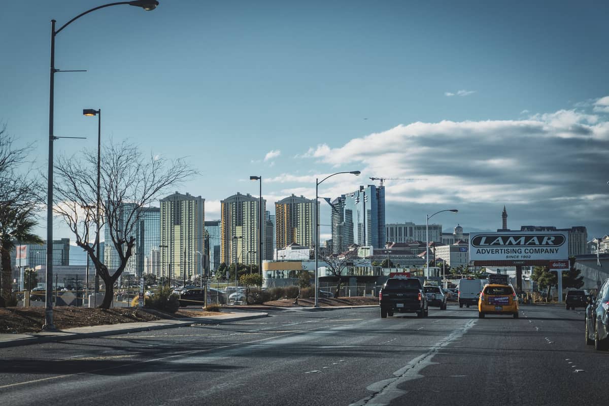Blick aus einem Auto, das auf die Skyline des Las Vegas Strip zufährt, mit Hotels und einem gelben Taxi im Vordergrund.