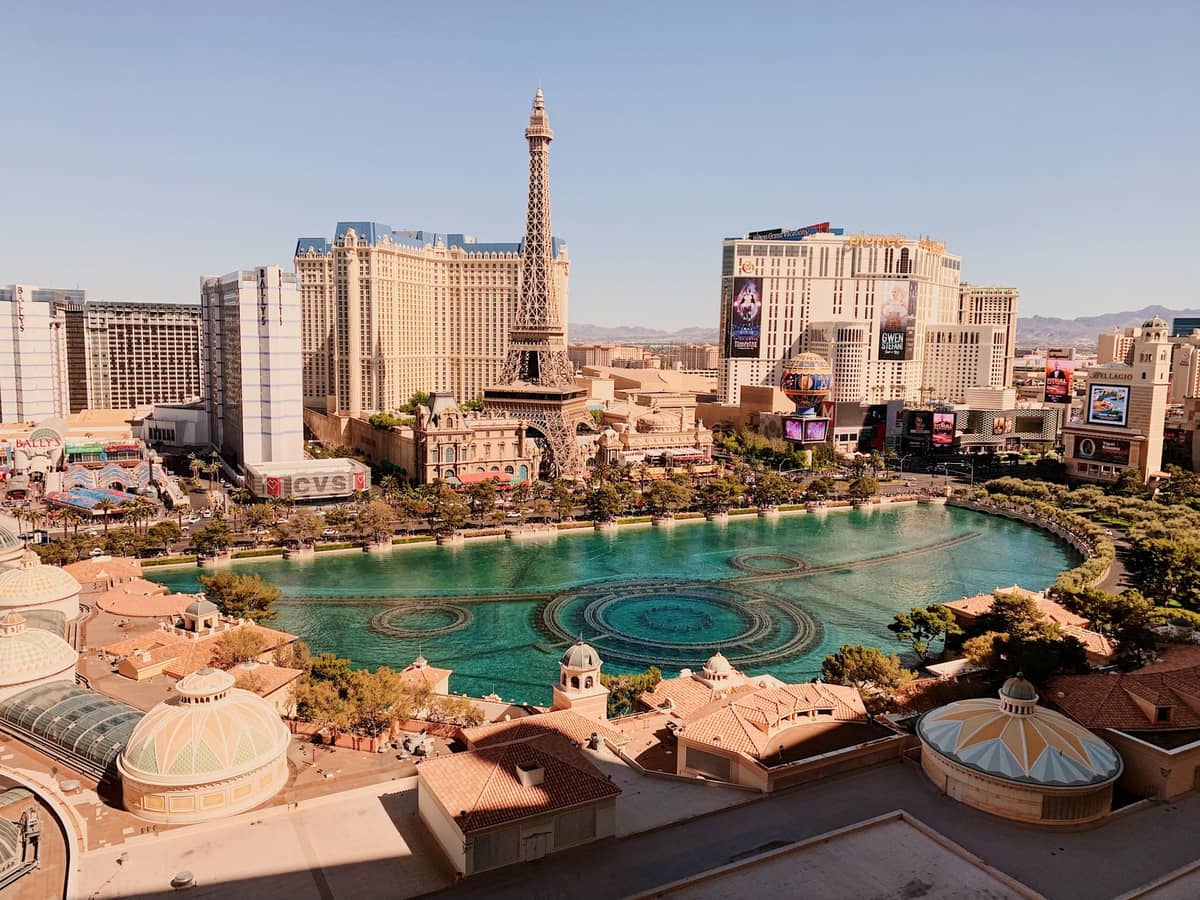Blick auf den Las Vegas Strip bei Tag mit Hotelresorts, dem Eiffelturm-Nachbau und den Bellagio-Fontänen vor einem klaren Himmel.