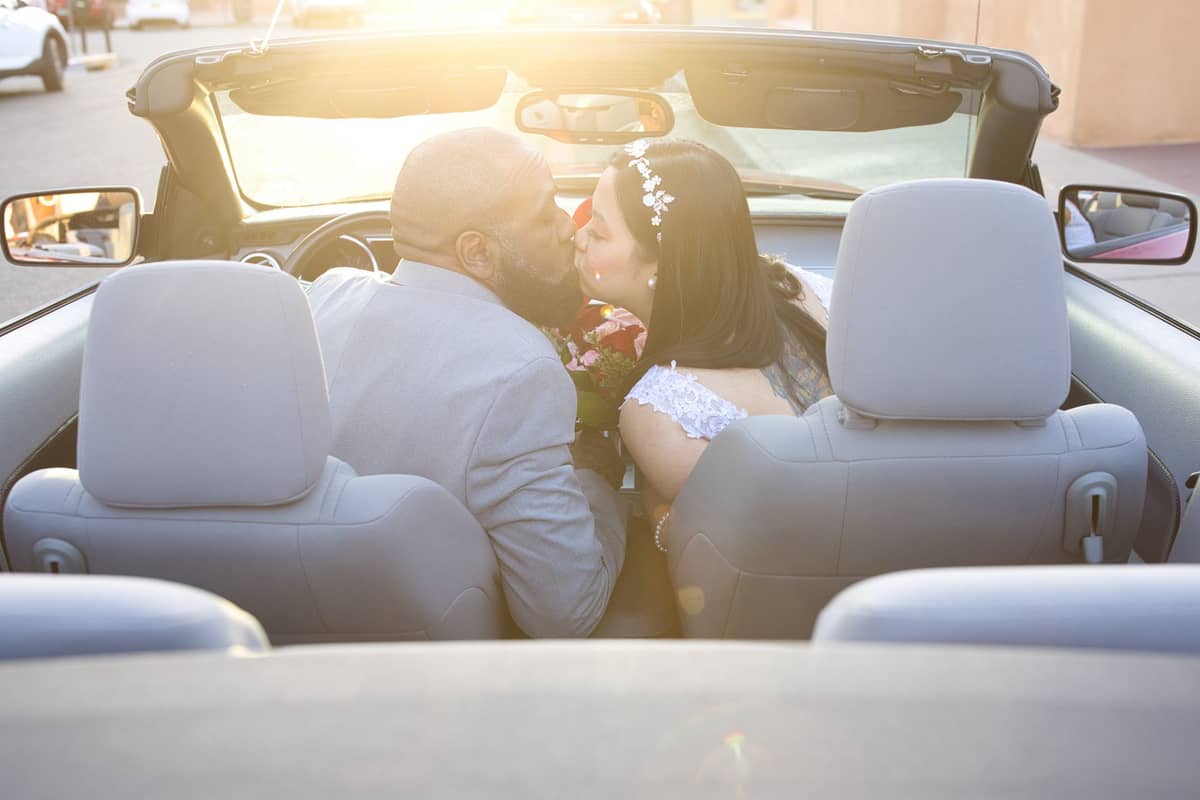 Les mariés s'embrassent dans une voiture décapotable, en référence aux chapelles de mariage drive-through de Las Vegas au coucher du soleil.