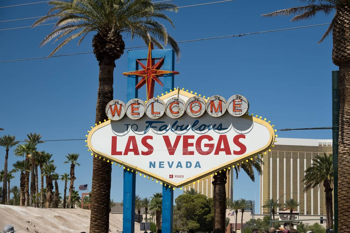 The iconic Welcome to Fabulous Las Vegas, Nevada sign on the Strip with palm trees and Mandalay Bay in the background under a clear blue sky.