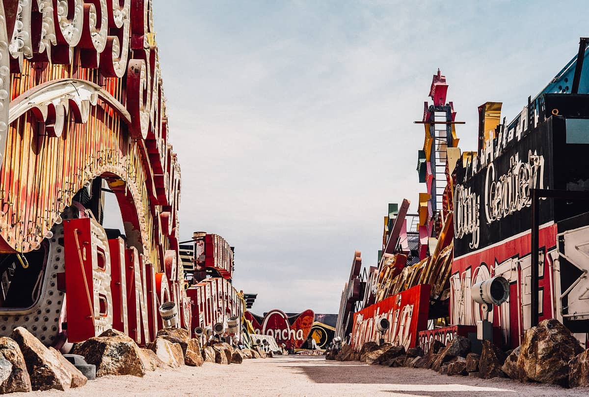 Rows of colorful vintage neon signs outdoors at the Neon Museum in Las Vegas, with clear sky above and gravel path between the displays.