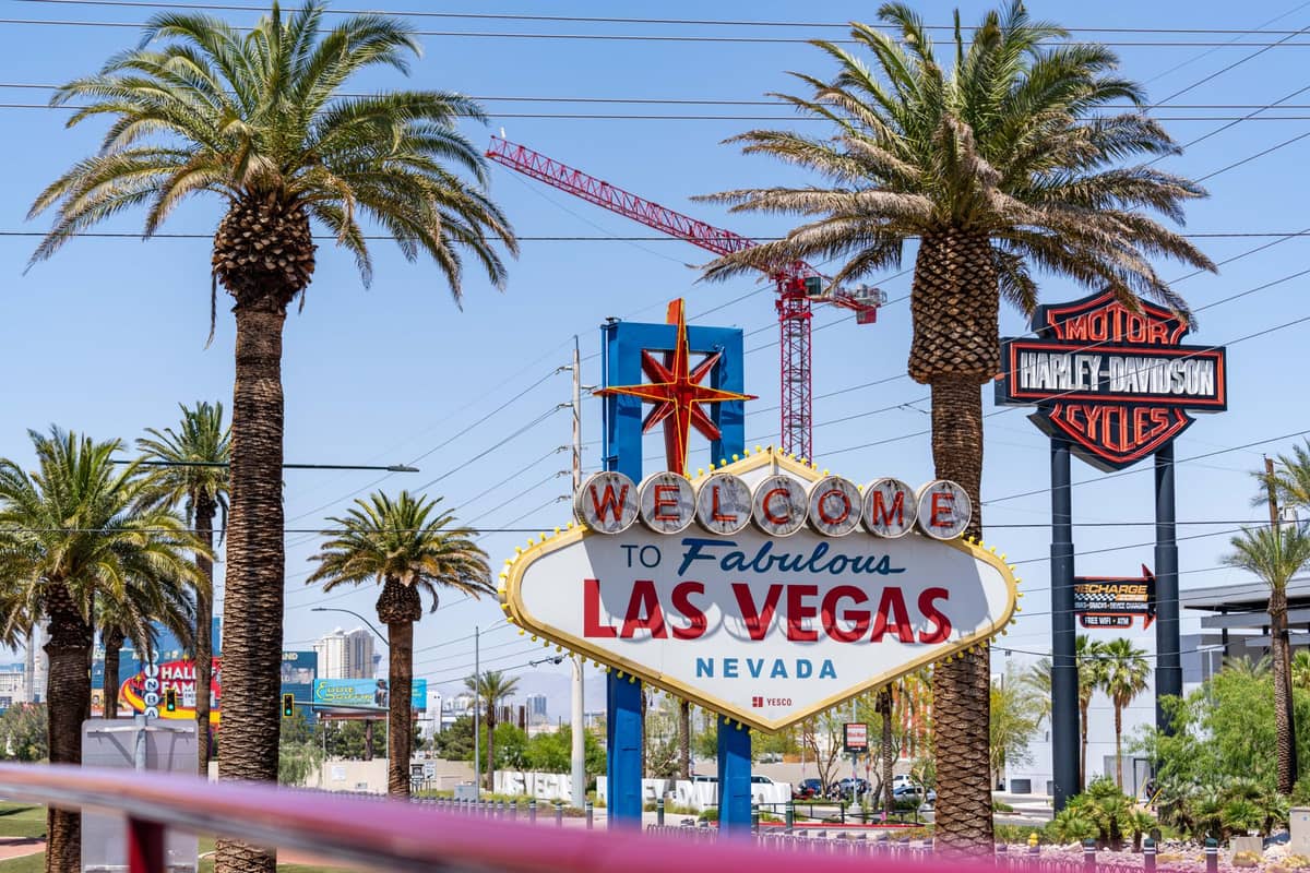 ป้ายชื่อดัง Welcome to Fabulous Las Vegas ที่ล้อมรอบด้วยต้นปาล์มในวันที่แดดส่องสวยท้องฟ้าสีฟ้าและเครนอยู่เบื้องหลัง