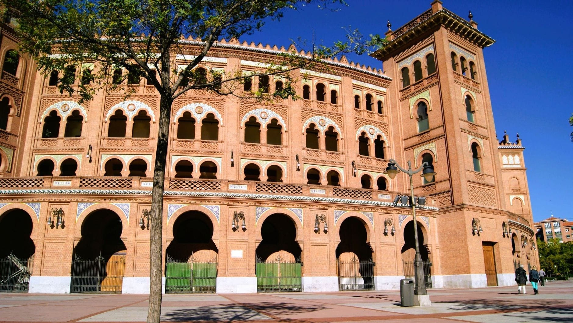 La grandiosa facciata in mattoni Neo-Mudéjar della Plaza de Toros de Las Ventas a Madrid, inondata di sole, con le sue arcate e un cielo azzurro limpido.