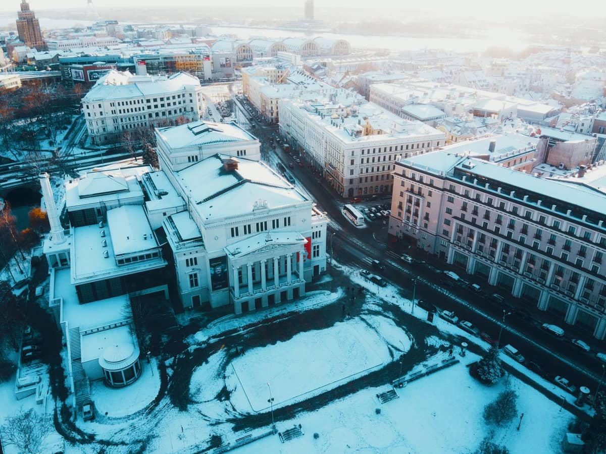 Winterliche Luftaufnahme des Lettischen Nationalen Opern- und Balletttheaters, umgeben von Schnee und Stadtstraßen im Zentrum von Riga.