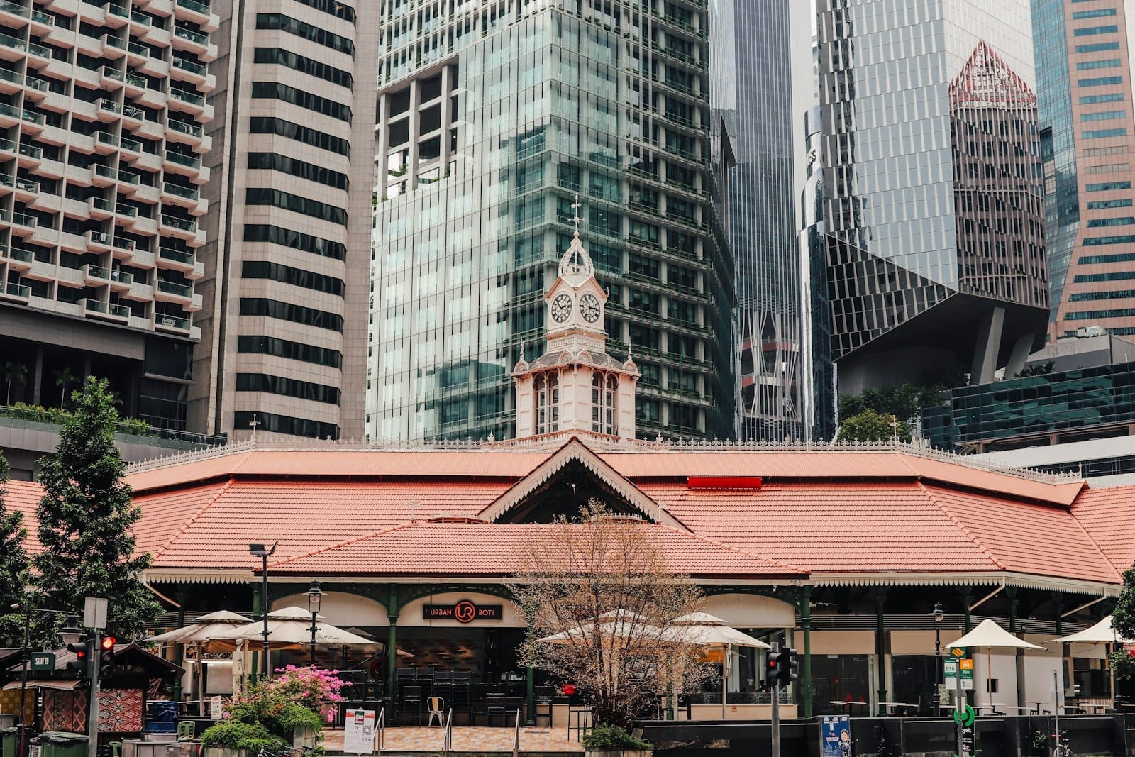 ภาพภายนอกอาคารตลาด Lau Pa Sat พร้อมหอนาฬิกาอันเป็นเอกลักษณ์ ตัดกับตึกระฟ้าสมัยใหม่ในย่านการเงินของสิงคโปร์