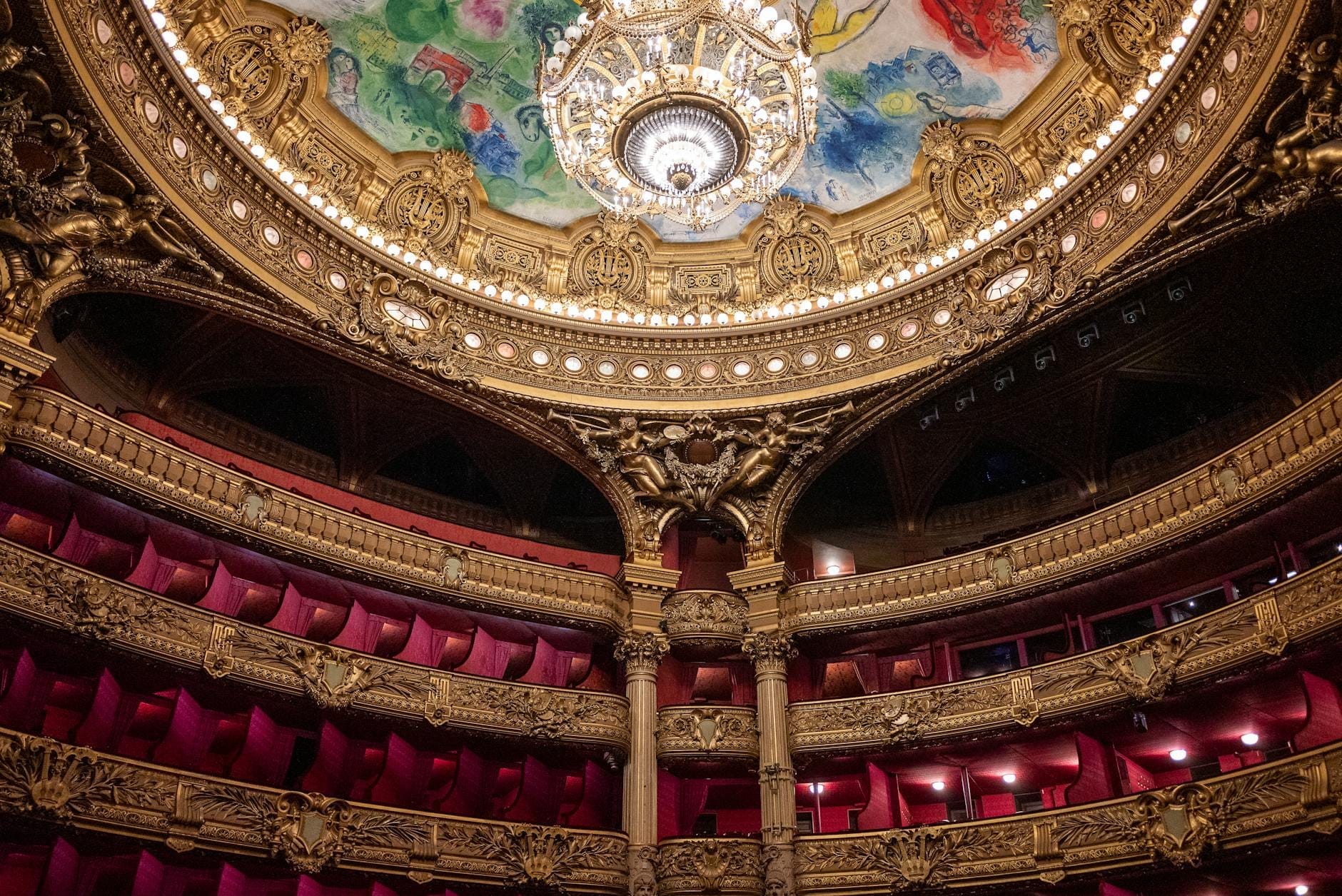 Interno opulento di un teatro Art Déco con poltrone in velluto rosso, balconi dorati decorati e un magnifico soffitto colorato con un lucente lampadario.