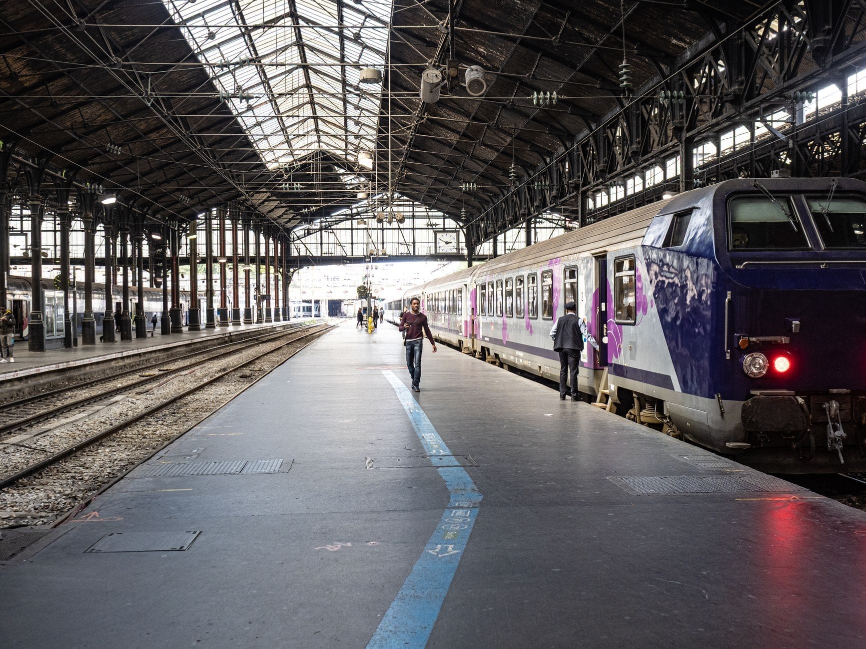 Pasajeros subiendo a un tren regional francés en una estación clásica con techo de cristal, ilustrando la logística de viaje en tren a Le Havre.