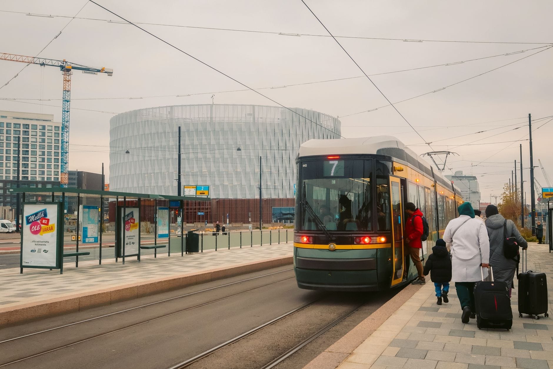 Bonde moderno chegando a uma parada da cidade com famílias e crianças embarcando, edifícios contemporâneos de Le Havre ao fundo.