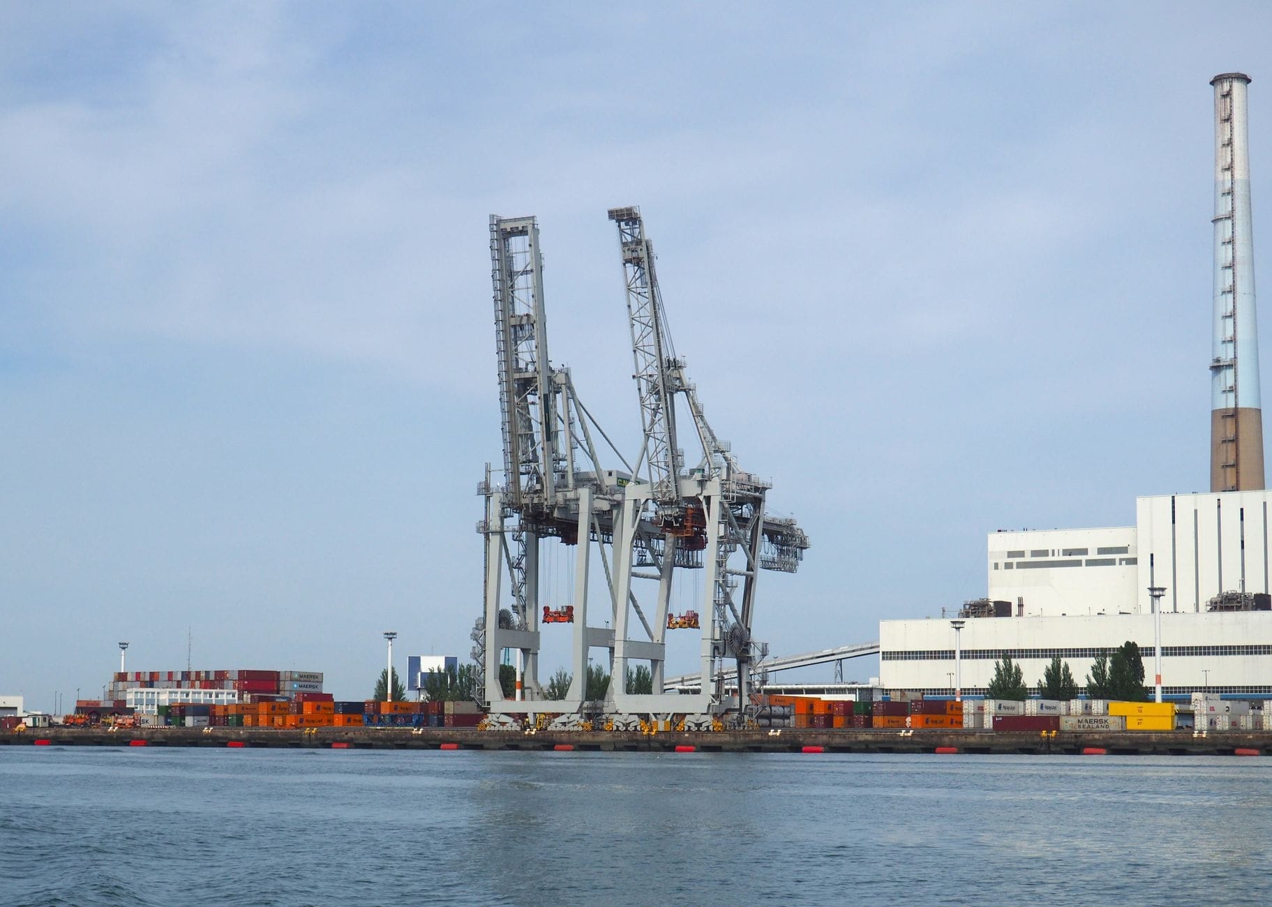 View of large industrial port cranes and shipping containers along the waterfront in Le Havre on a clear day.