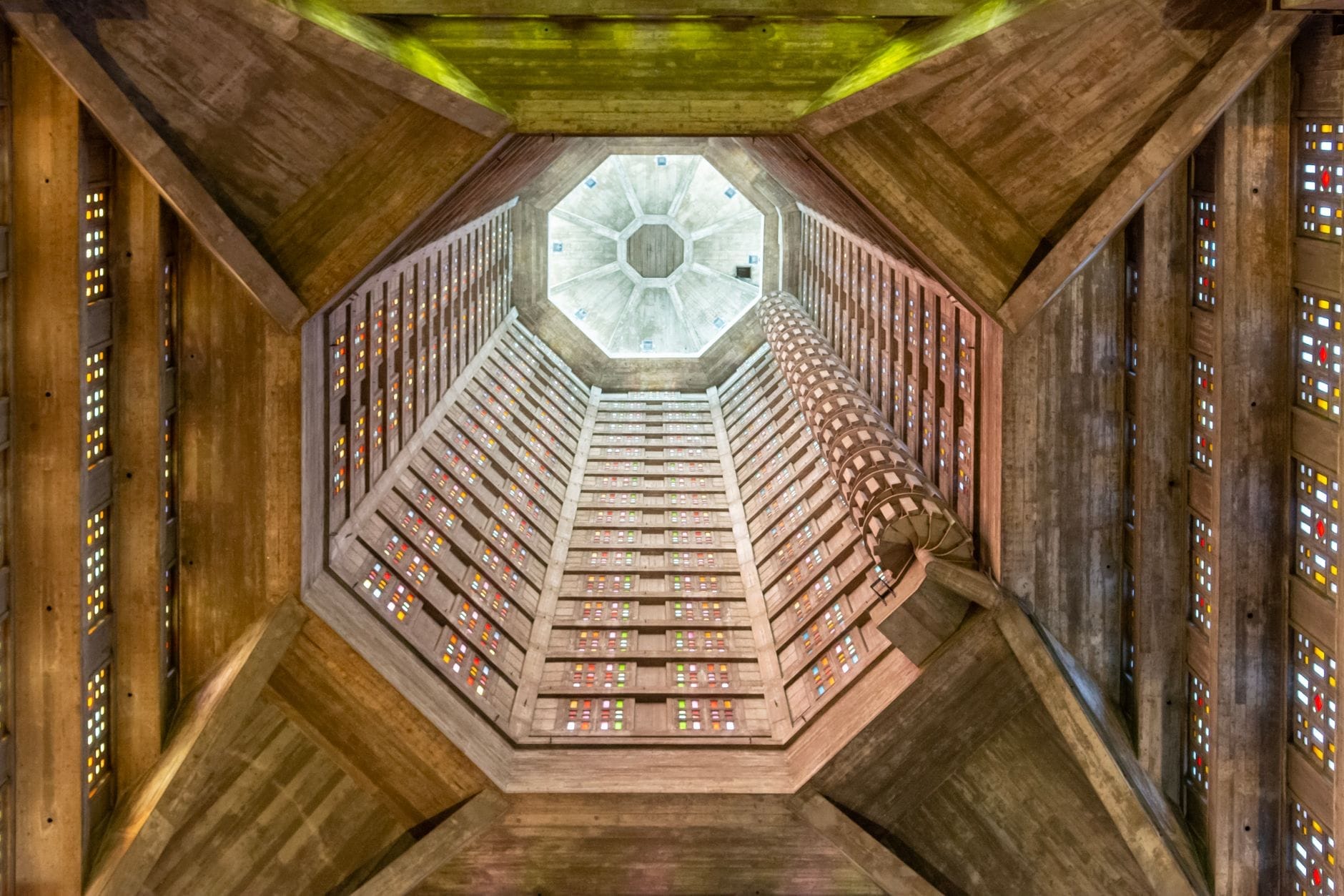 View looking up inside the octagonal concrete tower of Saint-Joseph Church in Le Havre, showing colored glass panels and dramatic geometric lines.