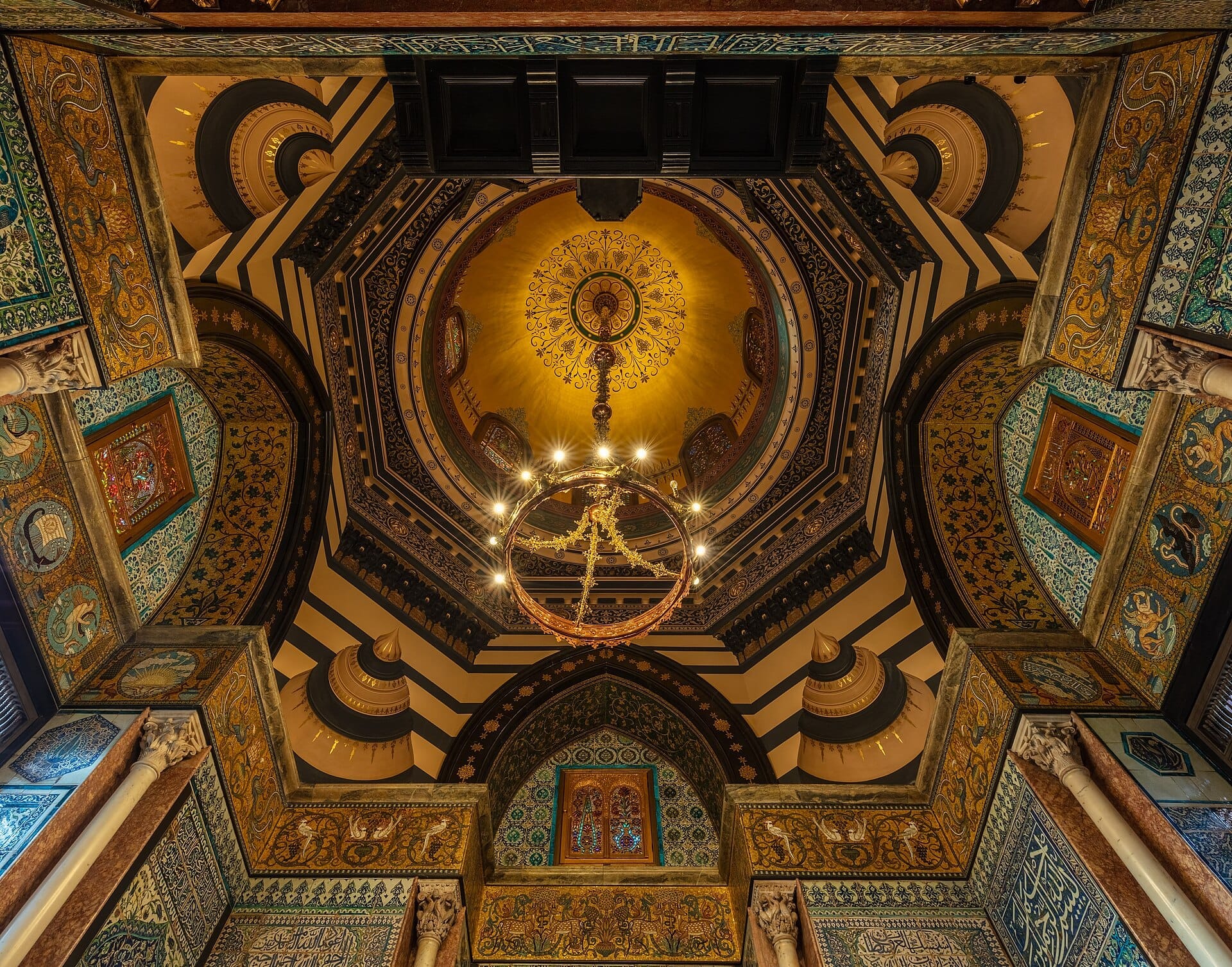 Soffitto a cupola ornato dell'Arab Hall al Leighton House Museum, con dettagli dorati, archi a strisce, piastrelle di Iznik e un lampadario centrale.