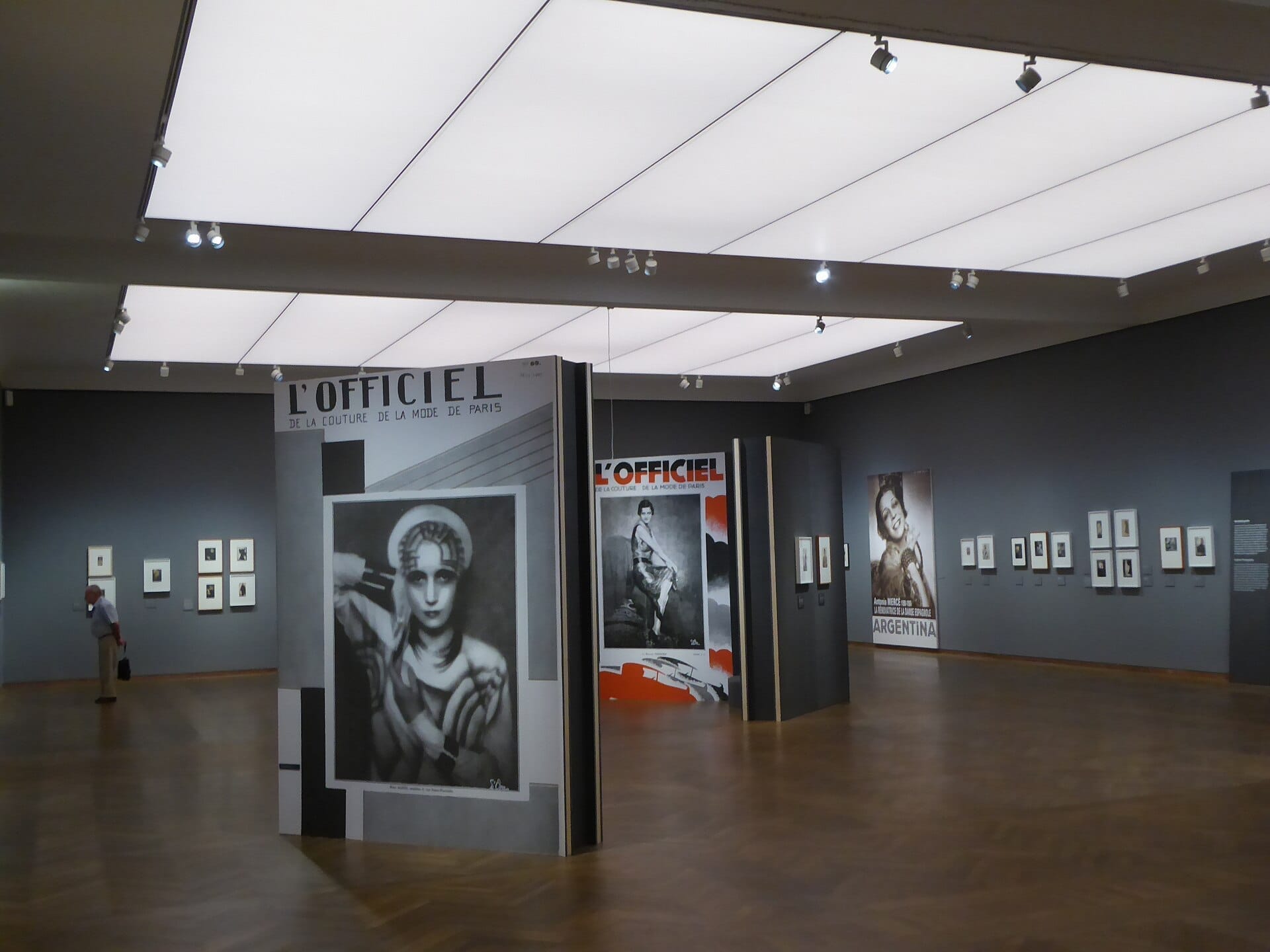 Geräumige Galerie im Inneren des Leopold Museum Wien mit modernen Kunstpostern, gerahmten Fotografien an grauen Wänden und einem einzelnen Besucher, der die Ausstellungsstücke betrachtet.