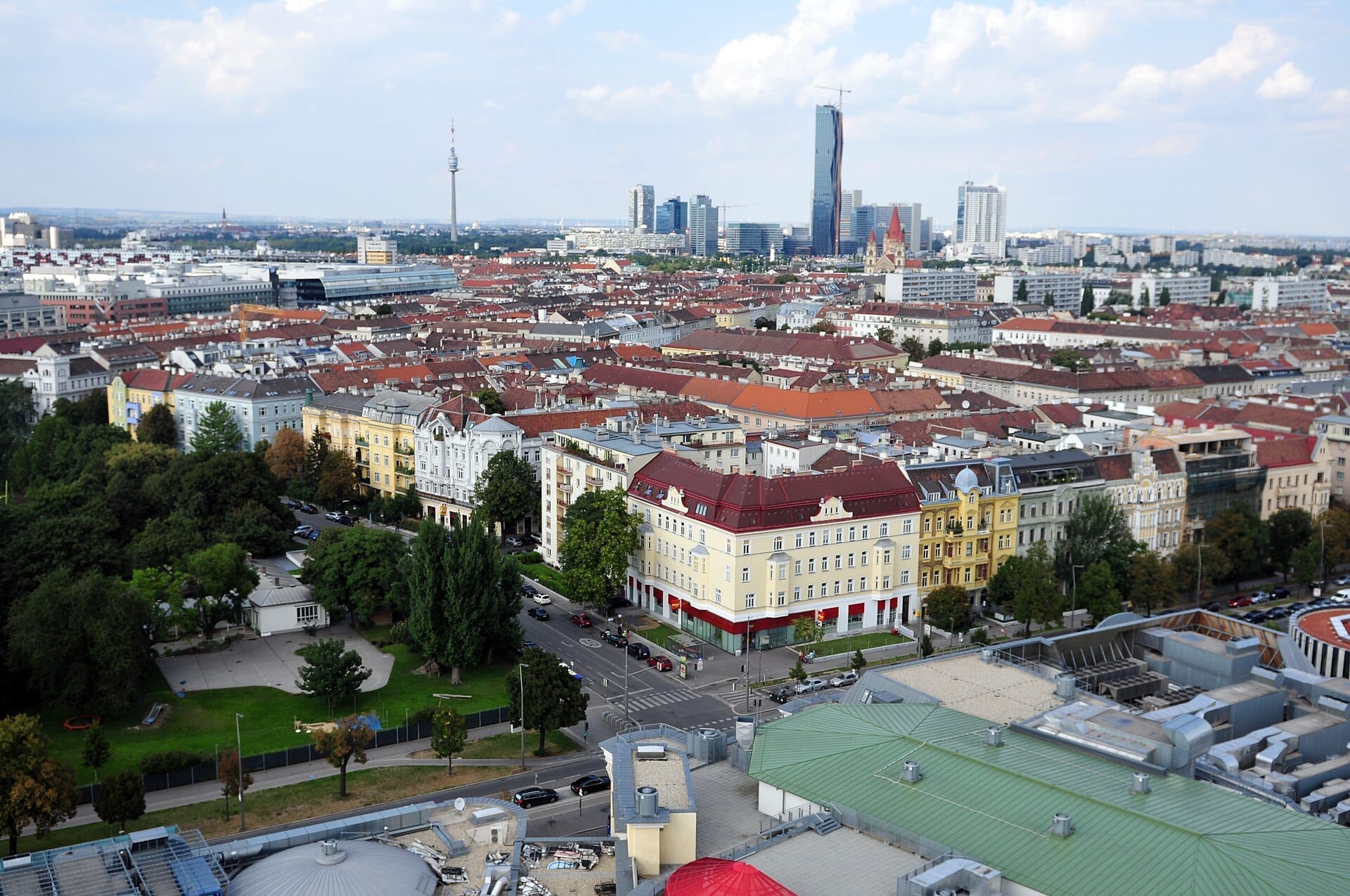 Luftaufnahme des Bezirks Leopoldstadt in Wien mit bunten historischen Gebäuden, baumgesäumten Straßen und modernen Wolkenkratzern unter einem teilweise bewölkten Himmel.