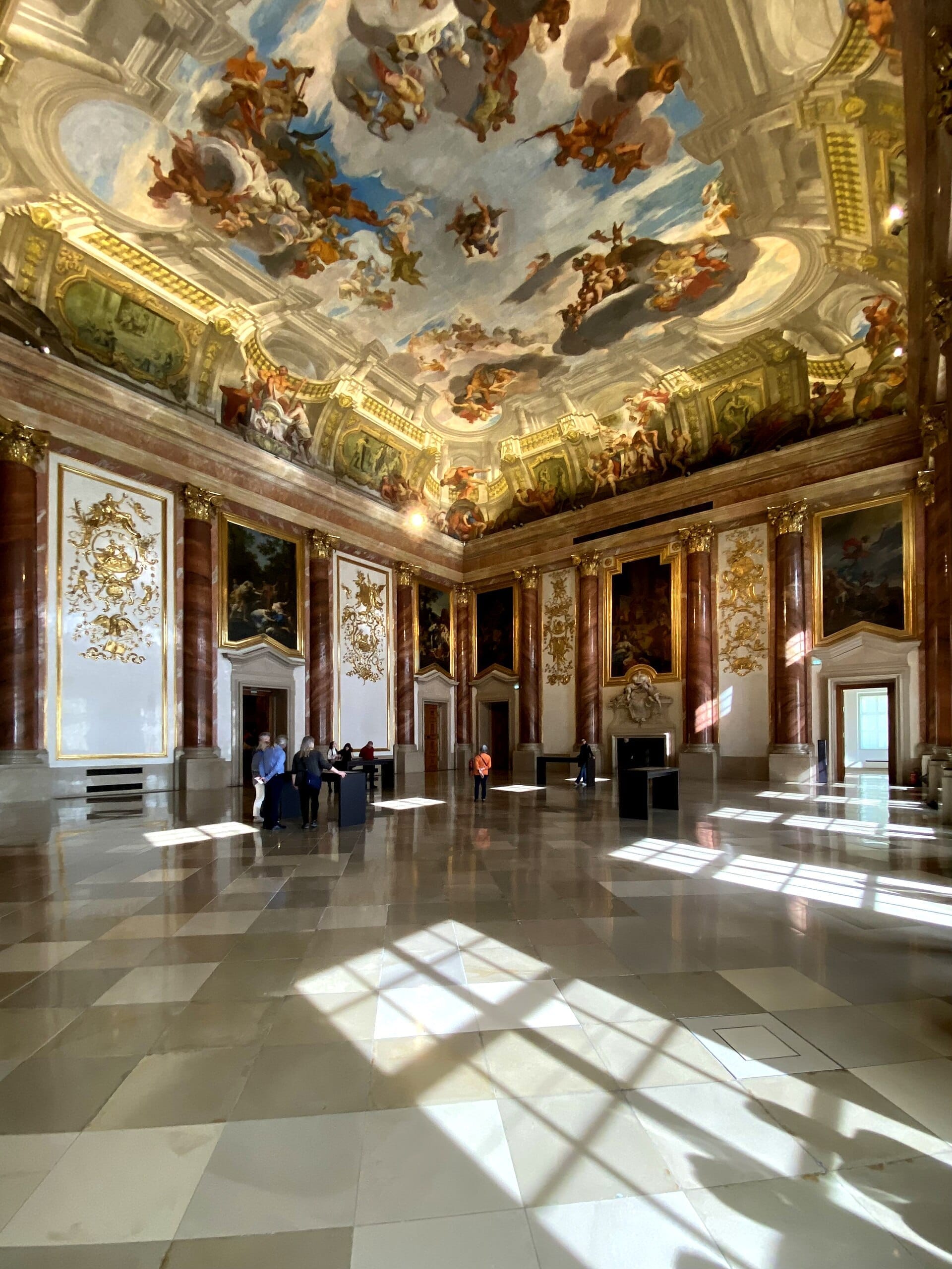 Barocksaal im Gartenpalais Liechtenstein in Wien mit verzierten Säulen, vergoldeten Details und einer prachtvollen bemalten Decke im Sonnenlicht.