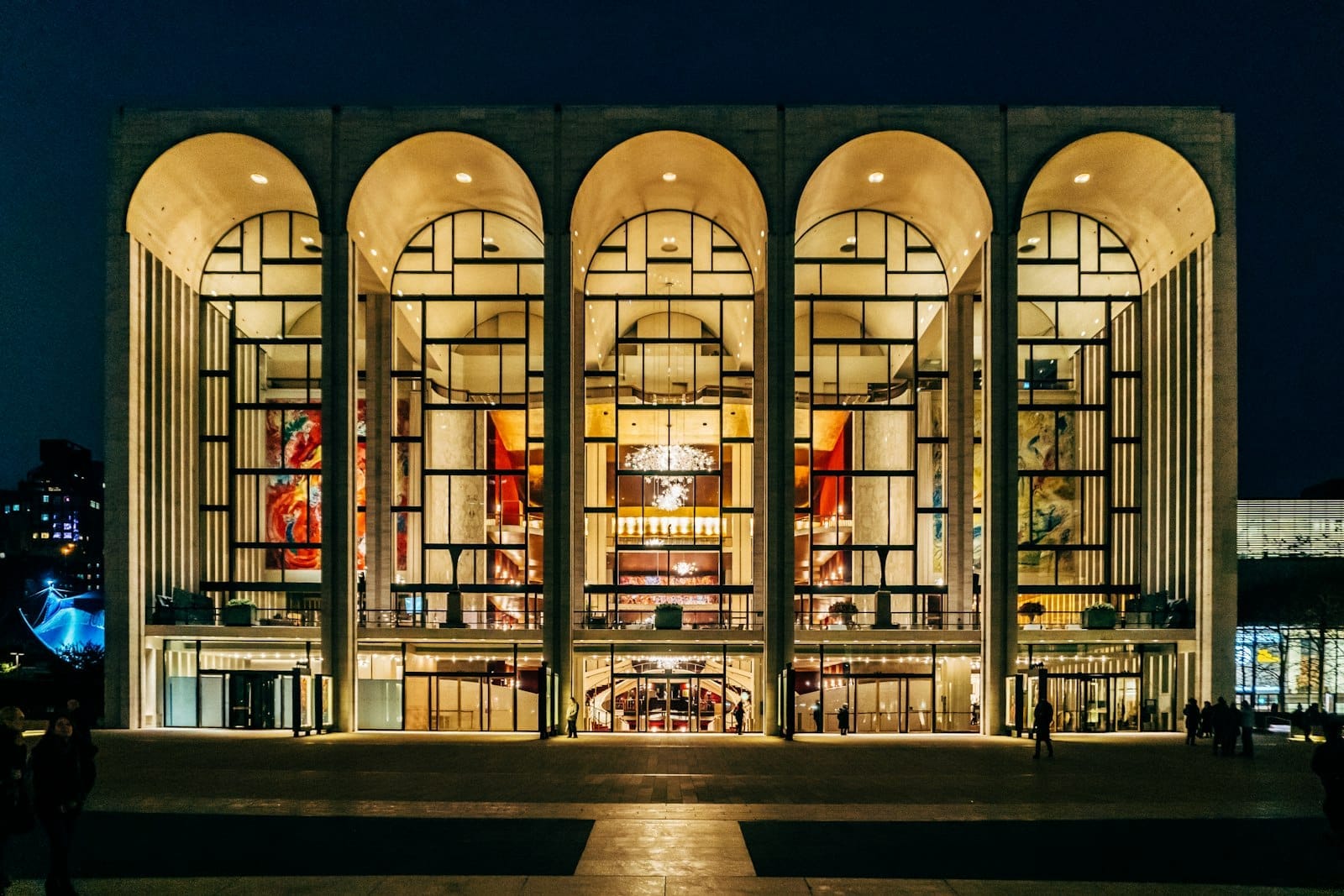 Vista esterna del Lincoln Center for the Performing Arts di notte, archi illuminati e grandi vetrate affacciate sulla piazza.