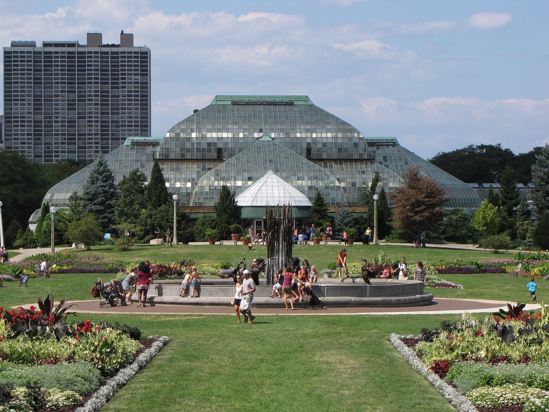 La caratteristica struttura vittoriana in vetro del Lincoln Park Conservatory circondata da giardini paesaggistici e visitatori affollati in un soleggiato pomeriggio a Chicago.