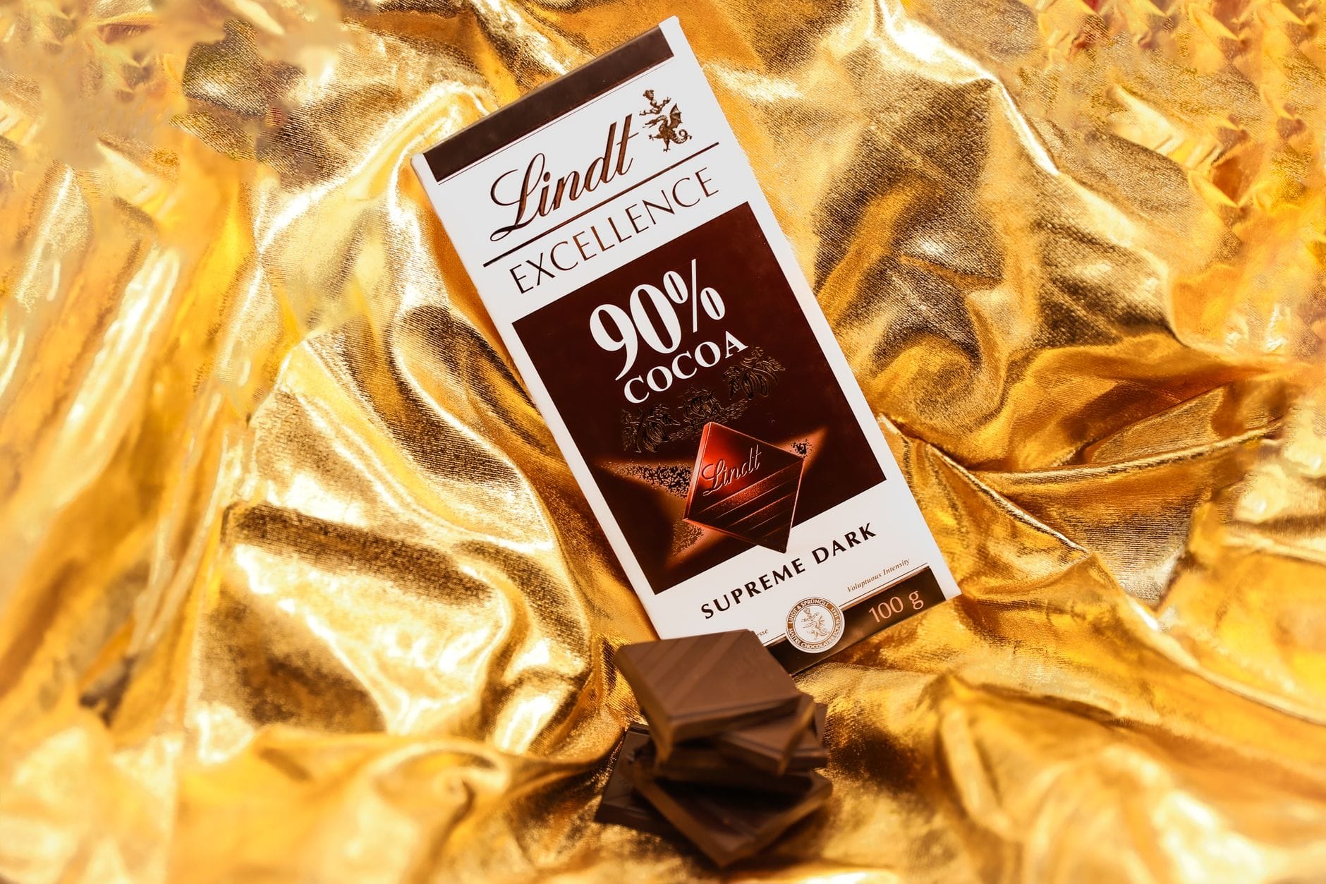แท่งช็อกโกแลต Lindt Excellence 90% Cocoa พร้อมชิ้นช็อกโกแลตวางบนพื้นฟอยล์สีทอง ภาพเน้นสินค้าชัดเจน ไม่ใช่พิพิธภัณฑ์