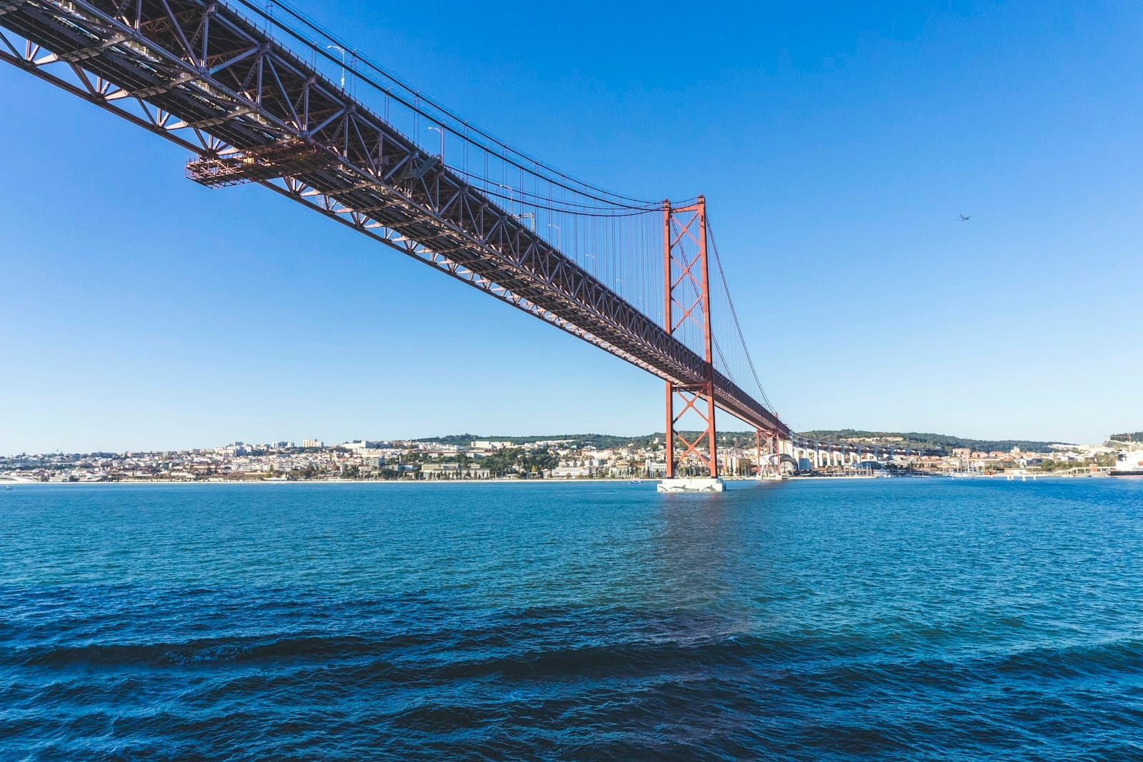Vue dramatique en contre-plongée du Pont 25 de Abril à Lisbonne montrant le pylône sud et l'eau en dessous par temps clair.