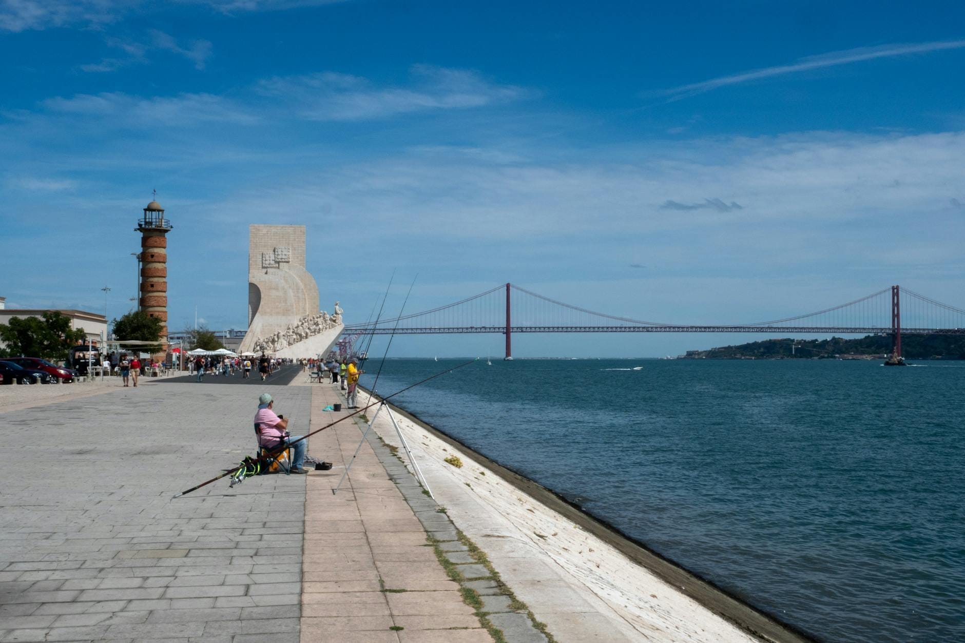 Front de mer de Lisbonne à Belém avec le Pont 25 de Abril, un phare et le Monument aux Découvertes visibles sous un ciel bleu.