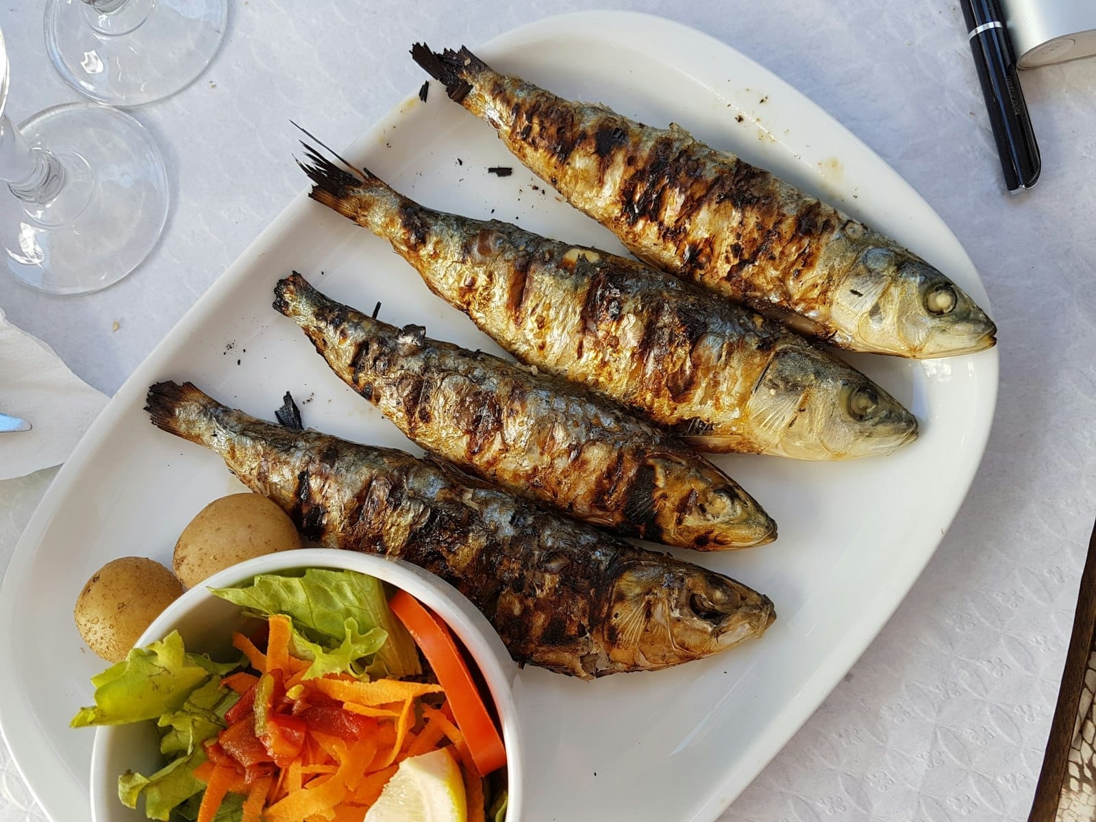 Prato com sardinhas grelhadas, salada e batatas sobre uma toalha de mesa branca, típico da cozinha de frutos do mar de Lisboa.