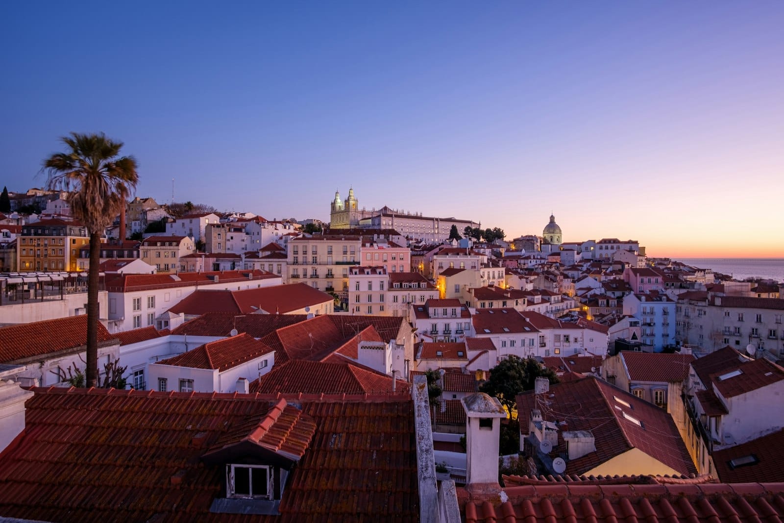 Vue du soir sur les toits de Lisbonne avec un ciel bleu profond et des lumières chaleureuses, capturant une atmosphère romantique au crépuscule.